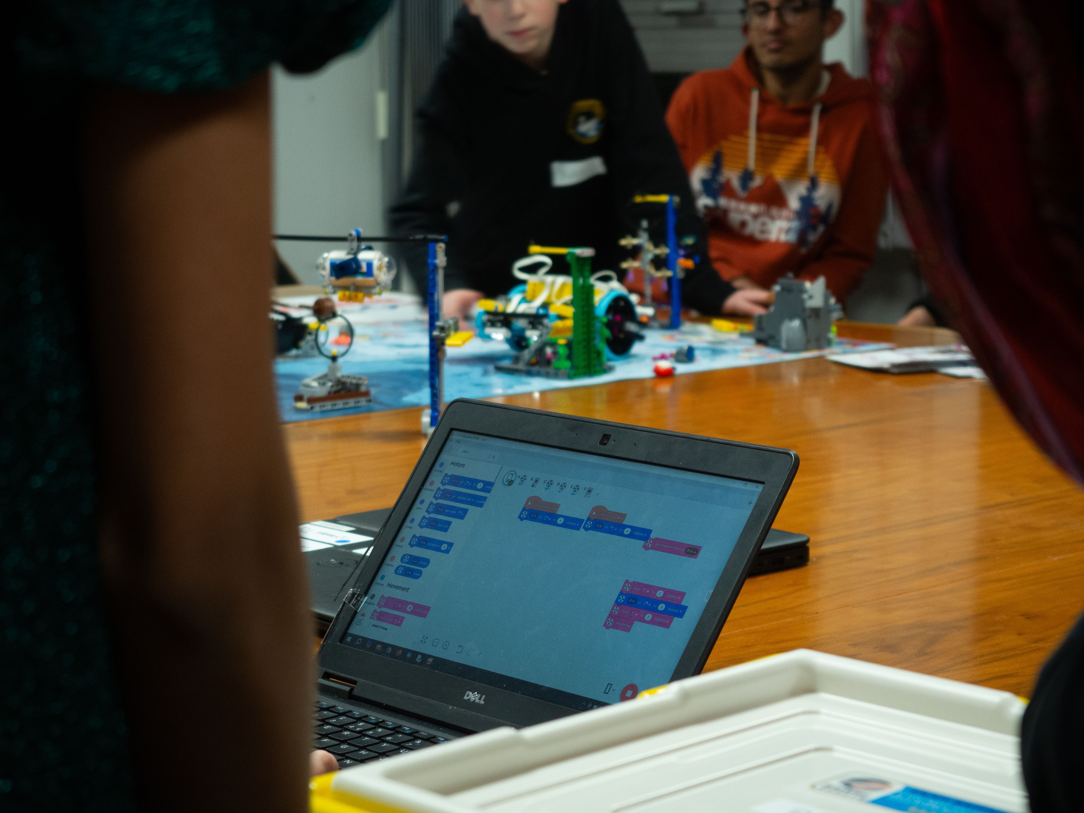 A laptop with block-based code to program a LEGO robot driving on a game mat around LEGO models