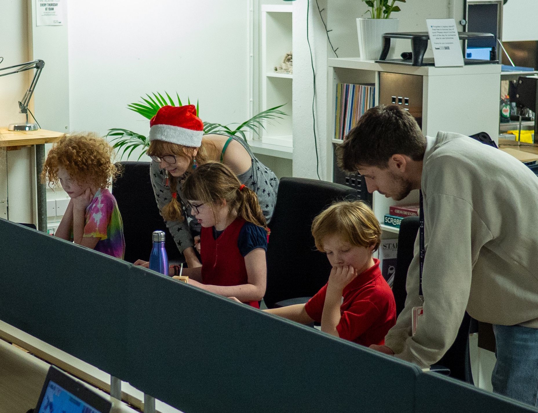 Two mentors are crouched down next to three attendees, looking at projects on their laptops together