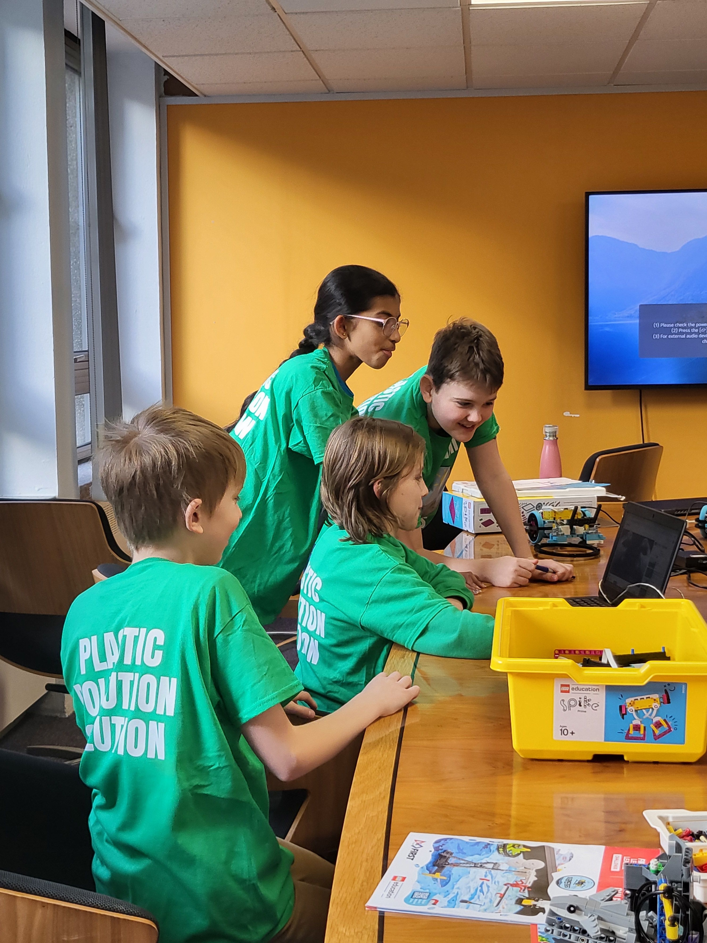 Four attendees wearing t-shirts that say 'Plastic Pollution Solution' huddled around a laptop surrounded by LEGO parts