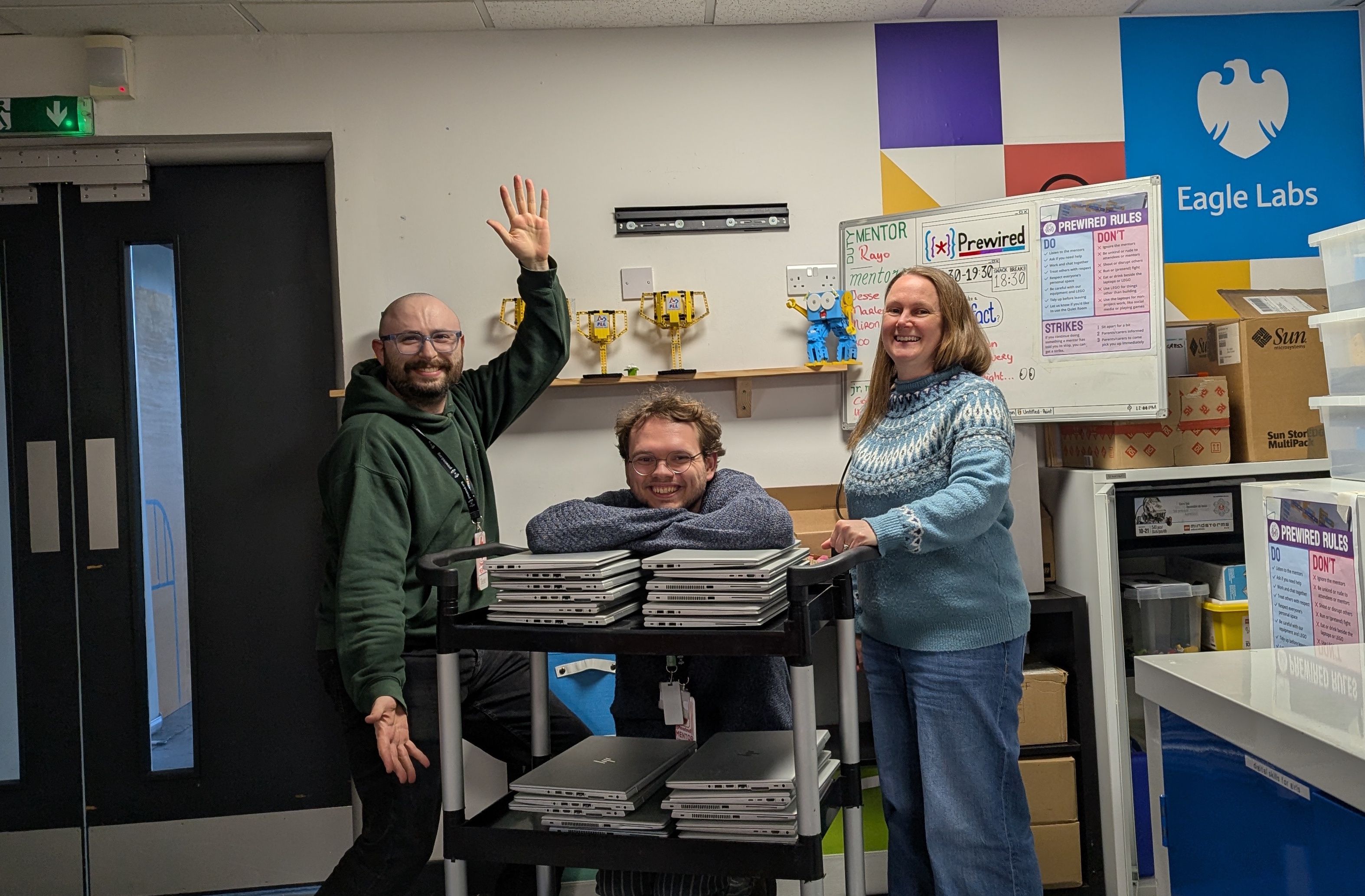 Three Prewired volunteers posing behind a trolley carrying 35 laptops
