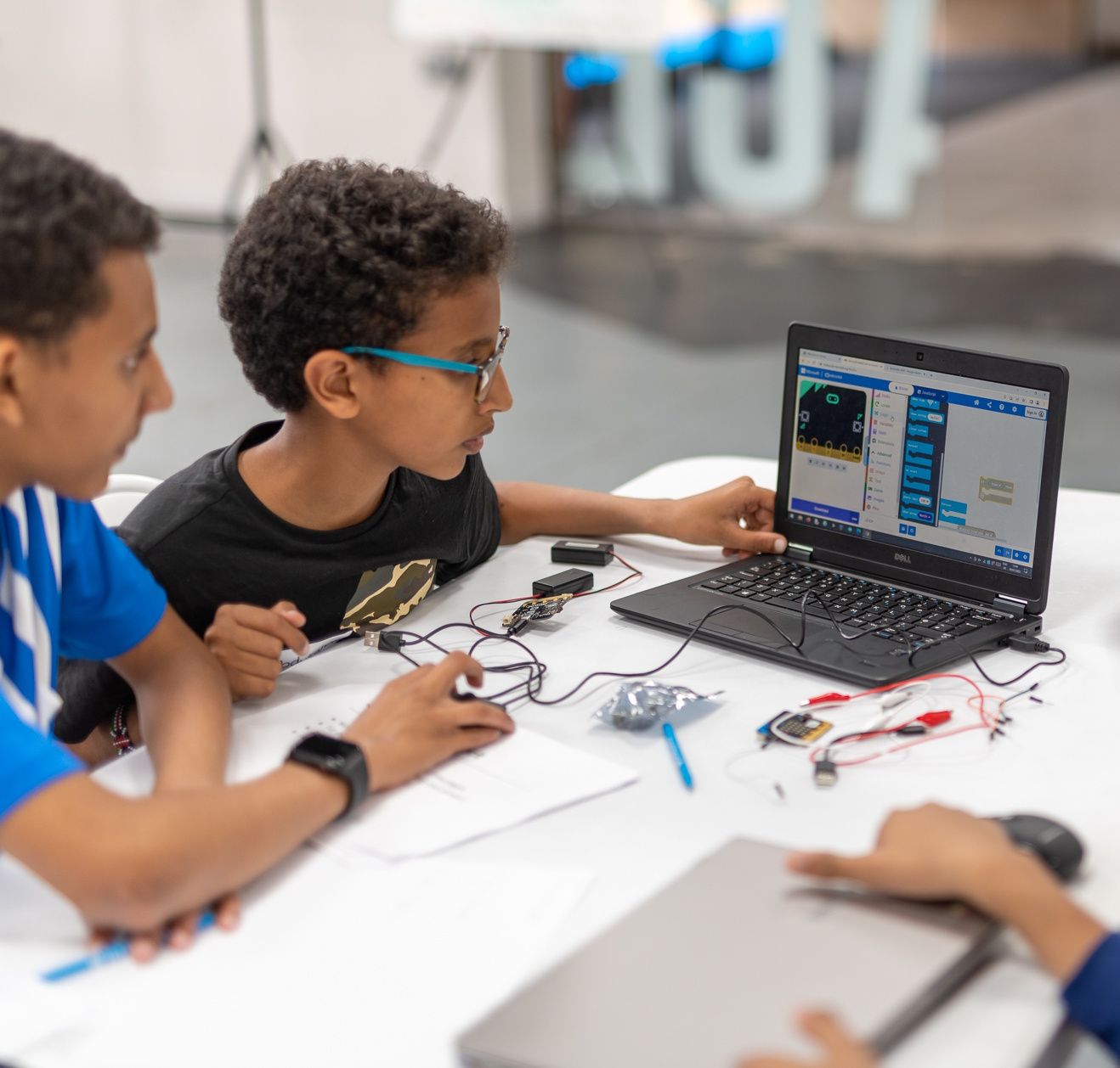Two attendees sitting behind a laptop, programming a BBC micro:bit connected to it